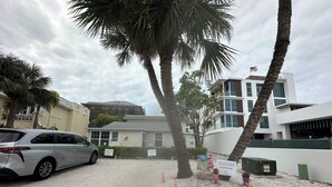 A parking area with a white car, palm trees, and a building with an American flag.