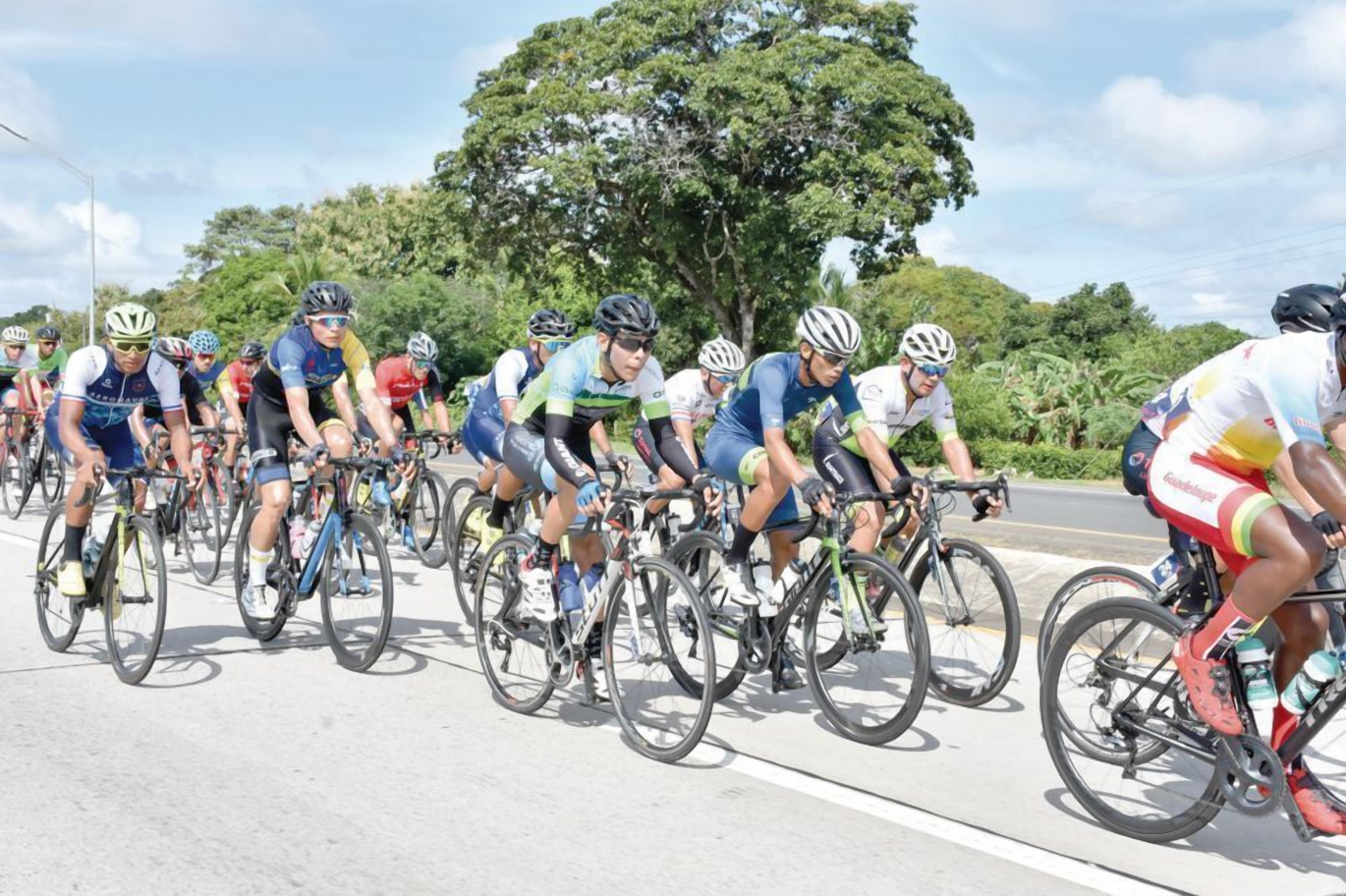 A group of cyclists riding on a road with trees and greenery in the background.