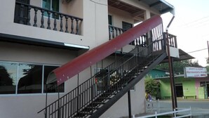 Un edificio con una escalera que lleva a un balcón, un cartel que indica estacionamiento privado, y un edificio verde al fondo.