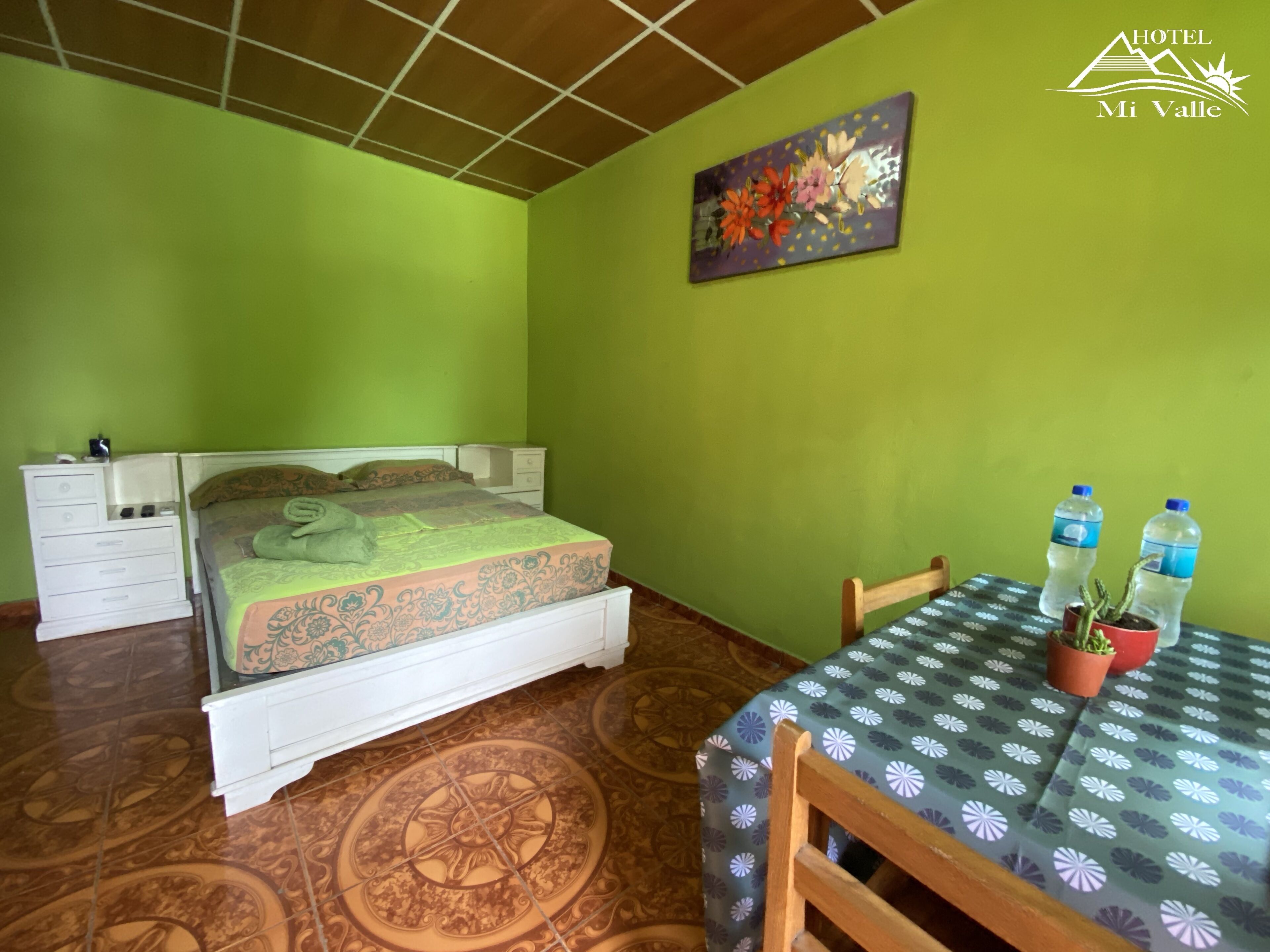 Una habitación de hotel con una cama, una mesita de noche, una mesa con una silla y una planta en maceta.