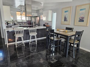 A modern kitchen with a central island, bar stools, and a dining table with chairs.