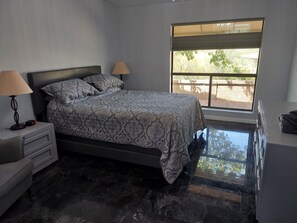 Ein Schlafzimmer mit Bett, Nachttischen, einer Lampe, einem Fenster mit Blick ins Freie und einem gefliesten Boden.