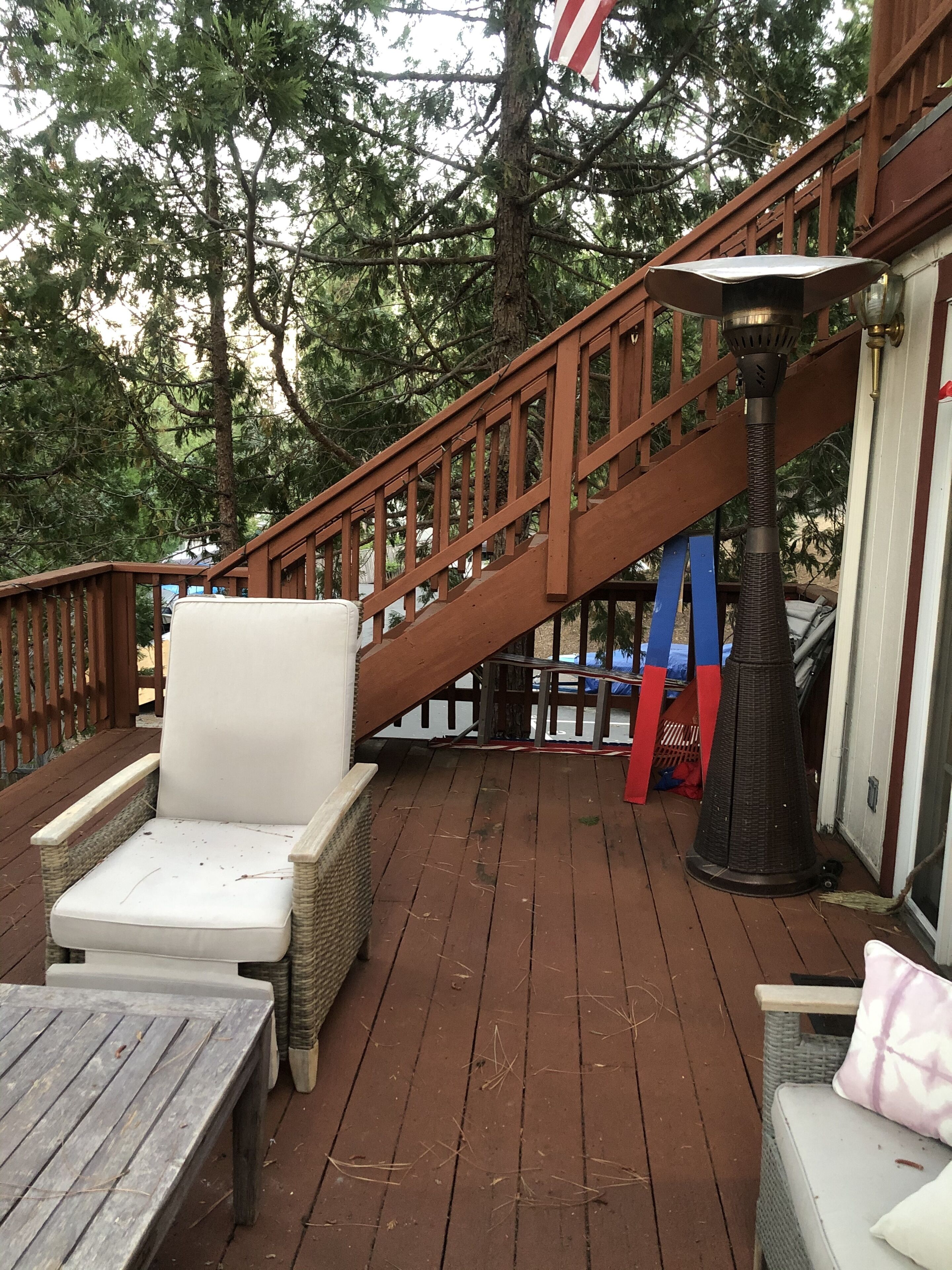 Eine Holzterrasse mit Gartenmöbeln, darunter ein Stuhl und ein Tisch, und eine Treppe, die zu einer erhöhten Ebene führt.