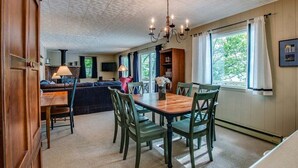 A dining area with a wooden table and chairs, a chandelier, and a view of the outdoors through large windows. - Bluff`s Charm 3 bedroom lake home on Keuka Lake (Penn Yan)