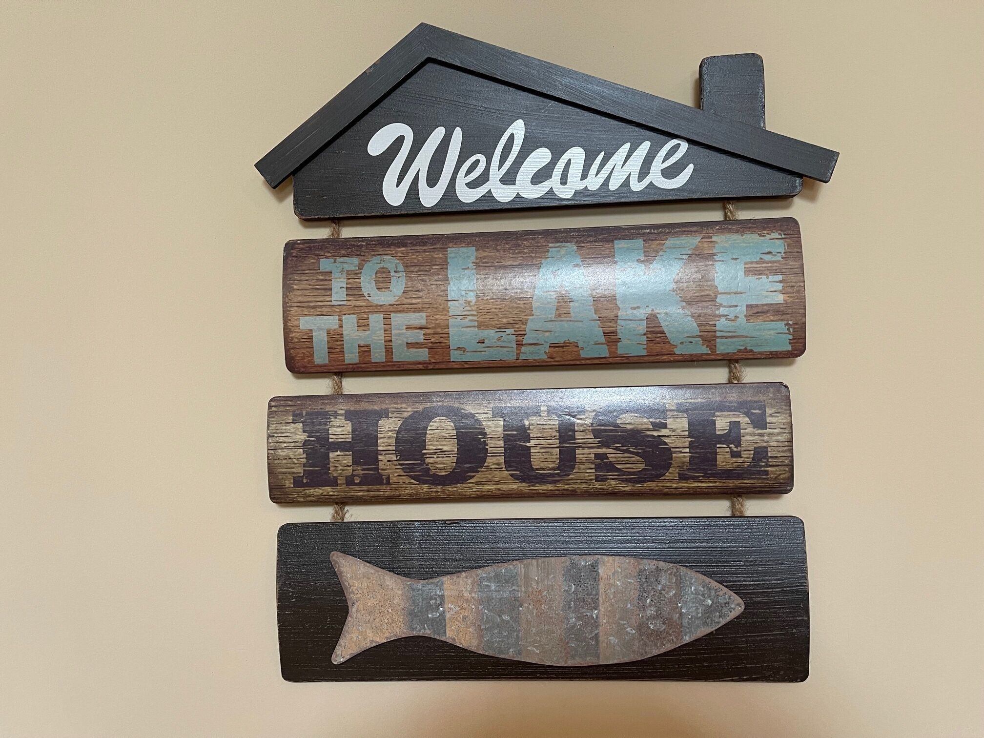 Decoración de pared con las palabras "Welcome to the Lake House" y un símbolo de pez.