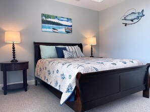 A bedroom with a bed, two bedside tables, a wall-mounted fish decoration, and a painting of a lake scene.