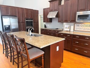 A kitchen with dark wooden cabinets, stainless steel appliances, a granite countertop, and a bar area with stools.