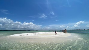 En strand med klart vand, sandet bred og en båd i det fjerne.