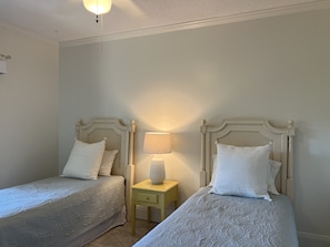 Deux lits simples avec des têtes de lit, une lampe de chevet et une petite table de chevet.