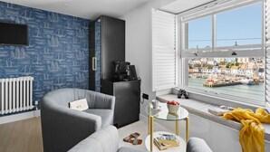 A modern living room with a view of a harbor, a gray sofa, a glass coffee table, and a black cabinet.