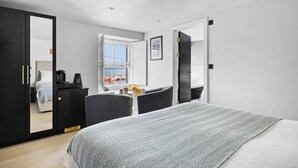 A modern bedroom with a bed, a desk, and a chair, a wardrobe, and a window with a view of boats.