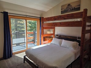 A bunk bed with a wooden headboard, a window with curtains, and a view of a deck.
