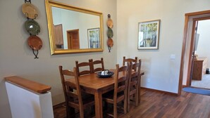 Ein Essbereich mit einem Holztisch, sechs Stühlen, einem kleinen Kühlschrank, einem großen Spiegel und zwei gerahmten Bildern an der Wand.