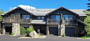 A two-story house with a stone foundation, multiple garage doors, and a balcony on the upper floor.