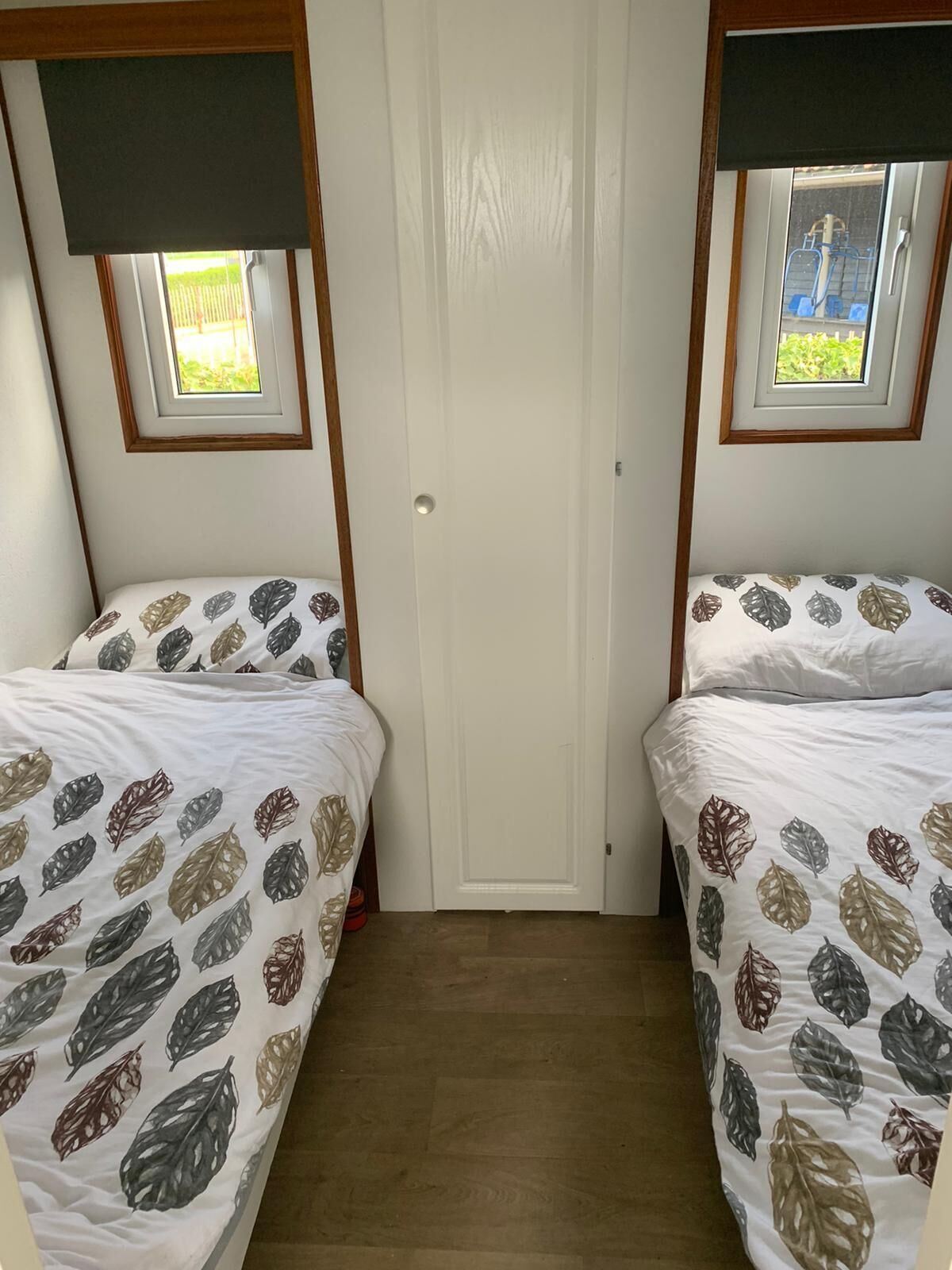 Ein Zimmer mit zwei Betten, jeweils mit blattgemusterten Bettbezügen, einem Holzboden und einer Tür mit Fenster darüber.