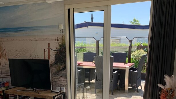 A living room with a TV, a sofa, a coffee table, and a sliding glass door leading to an outdoor patio with a table and chairs.