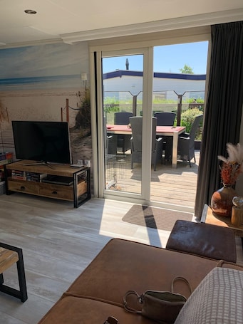 A living room with a TV, a sofa, a coffee table, and a sliding glass door leading to an outdoor patio with a table and chairs.