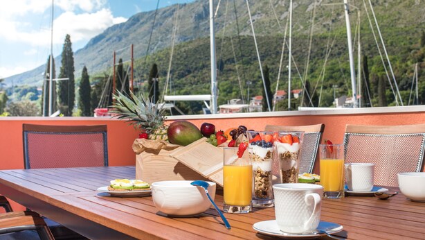 A table set with breakfast items including fruits, yogurt, and juice, overlooking a mountainous landscape with boats in the background. - Vitality Villa Mariante - free kayaks, private sauna (Komolac)