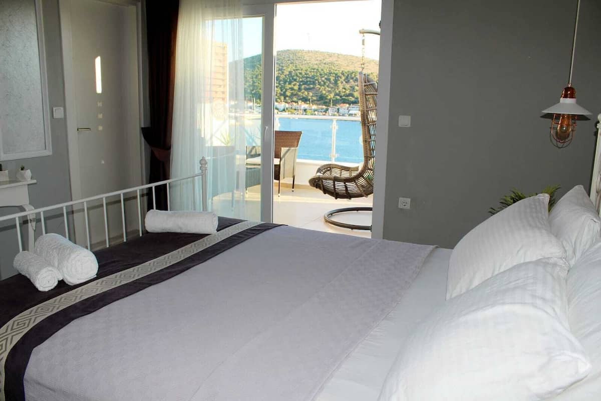 Una habitación de hotel con una cama grande, un balcón con vistas al mar y una silla de mimbre.