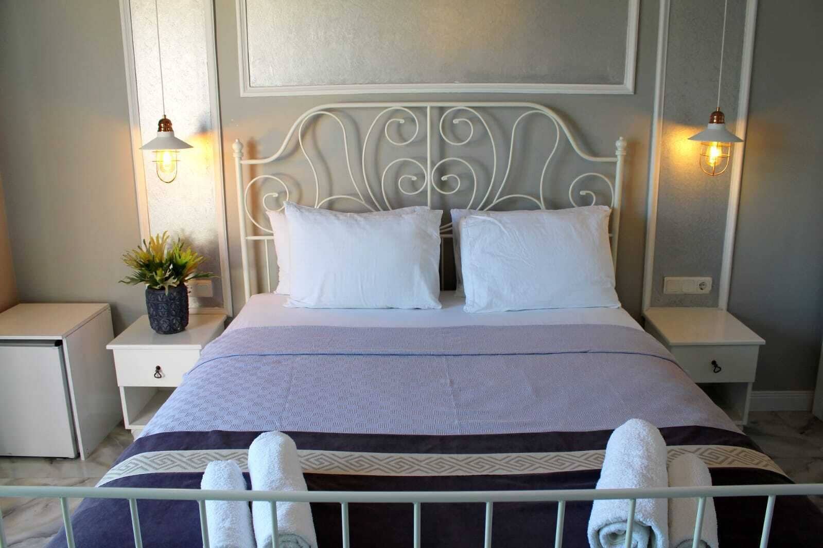 A neatly made bed with white linens, two bedside tables with lamps, and a potted plant on one table.