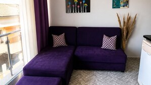 A modern living room with a sectional sofa, a wooden coffee table, and a small kitchen area. - Viya Plus Cesme (Cesme)