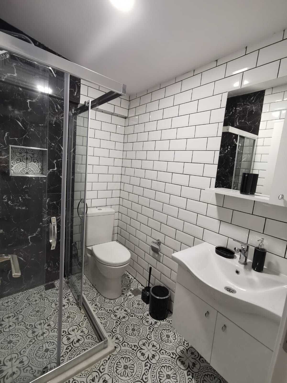 A bathroom with white subway tiles, a black marble shower enclosure, a white toilet, and a white sink with a mirror above it.