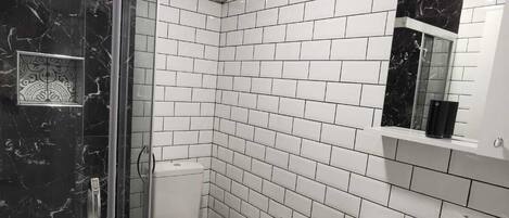 A bathroom with white subway tiles, a black marble shower enclosure, a white toilet, and a white sink with a mirror above it.