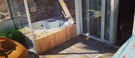 A sunlit patio with a hot tub, a lounge chair, and a thatched roof structure.