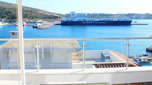 Un balcon avec un parasol blanc, une table et des chaises donnant sur une marina où est amarré un grand navire appelé « ULUSOY Sealios ».