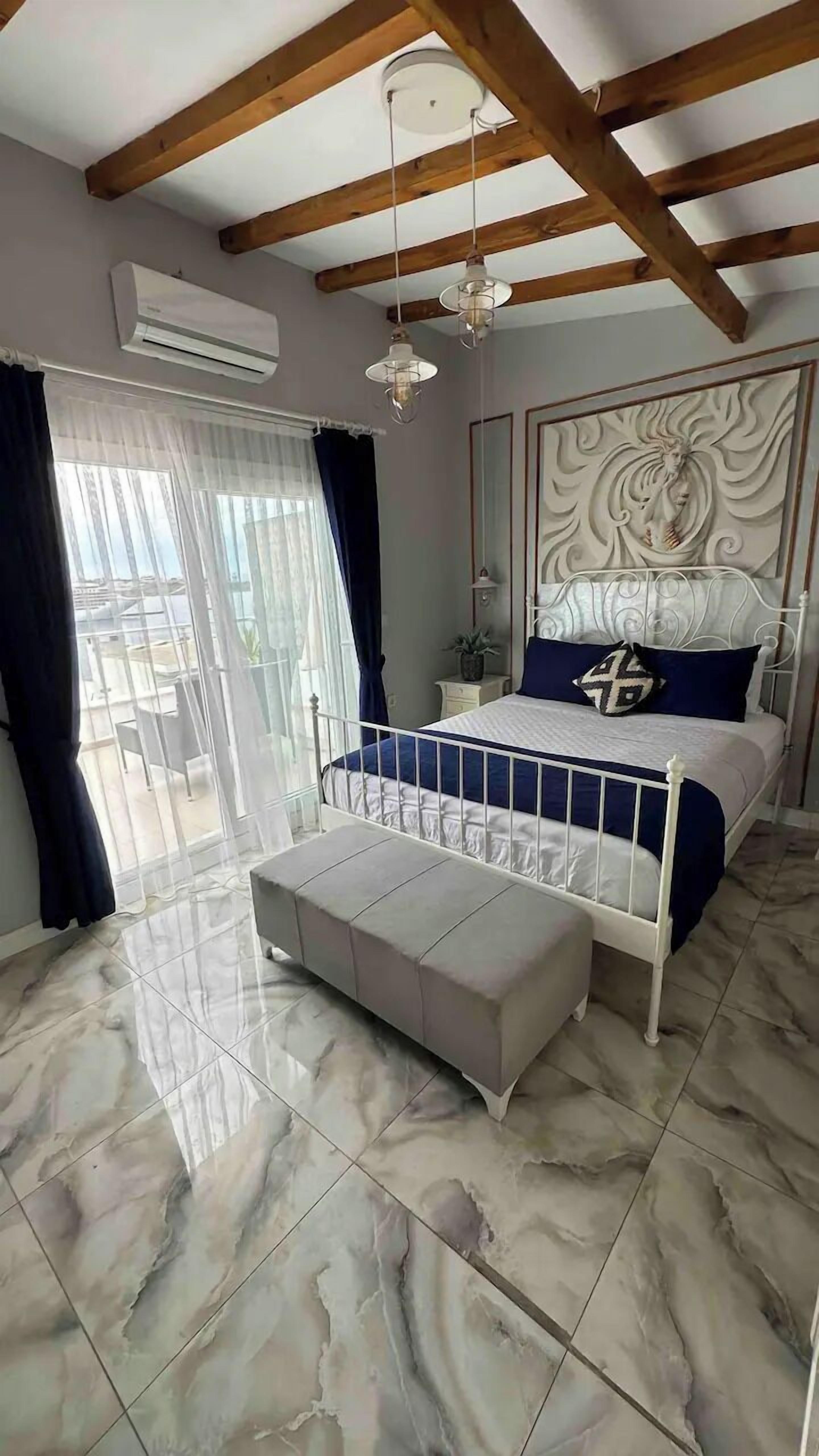 Un dormitorio con cama, un banco, ventilador de techo y ventana con cortinas.
