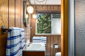 A wooden-paneled bathroom with a large window, a white sink, and striped towels. - Hawk's Haven (Tahoe Vista)