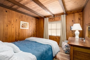 A wooden-paneled room with a bed, a desk, and a window with curtains. - Hawk's Haven (Tahoe Vista)