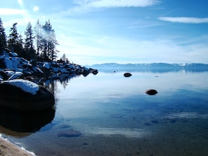 A calm lake with snow-covered rocks and trees in the background. - Hawk's Haven (Tahoe Vista)