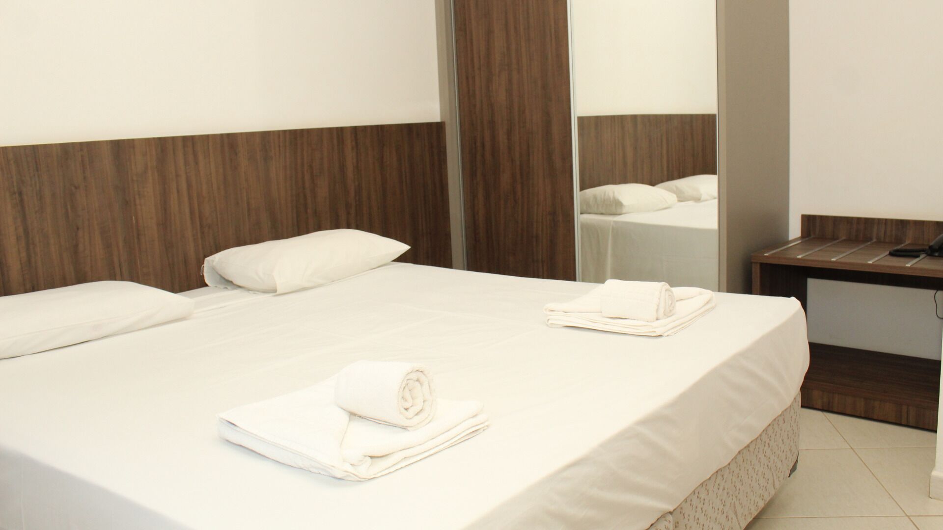 A hotel room with a large bed, a wooden headboard, a bedside table, and a mirror.