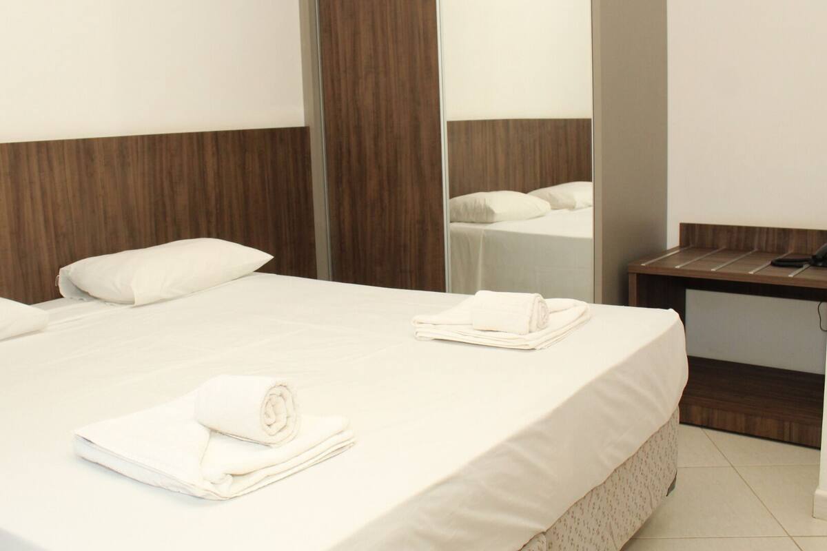 A hotel room with a large bed, a wooden headboard, a bedside table, and a mirror.