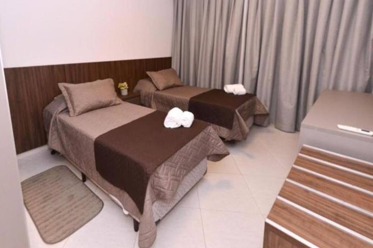 A hotel room with two beds, a sofa, a small table, and a curtain.