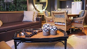 A living room with a brown sofa, wicker chairs, a coffee table, and a kitchen area in the background. - Barretos Park Hotel (Barretos)
