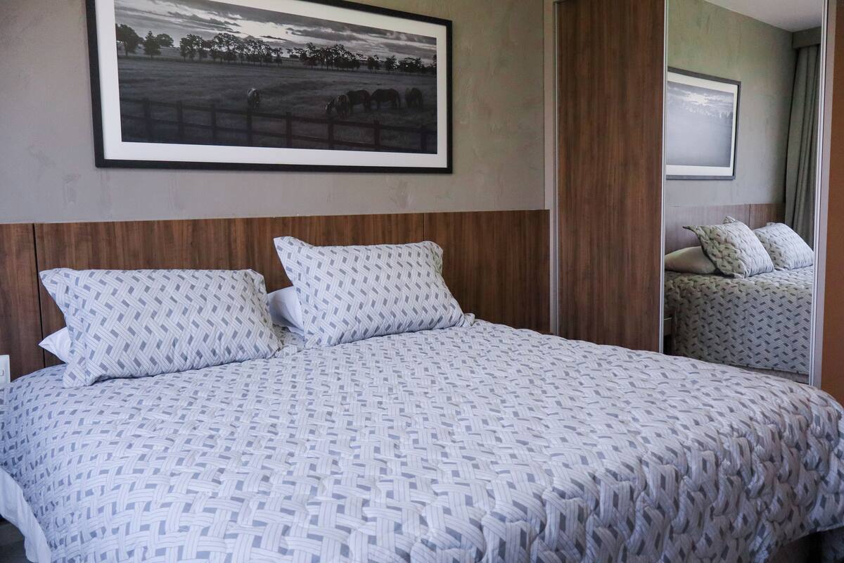 A hotel room with a large bed, a framed picture on the wall, and a mirror reflecting the bed.