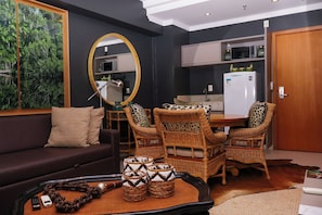 A living room with a sofa, chairs, a coffee table, a mirror, and a kitchen area with a refrigerator. - Barretos Park Hotel (Barretos)