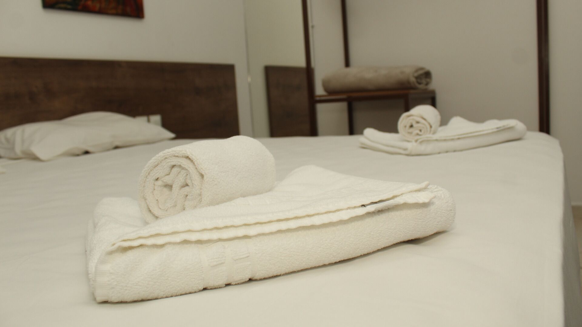 A hotel room with a neatly made bed, a wooden headboard, and a small table with a rolled towel.