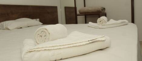 A hotel room with a neatly made bed, a wooden headboard, and a small table with a rolled towel.