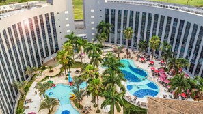 A hotel with multiple swimming pools, palm trees, and outdoor seating areas.