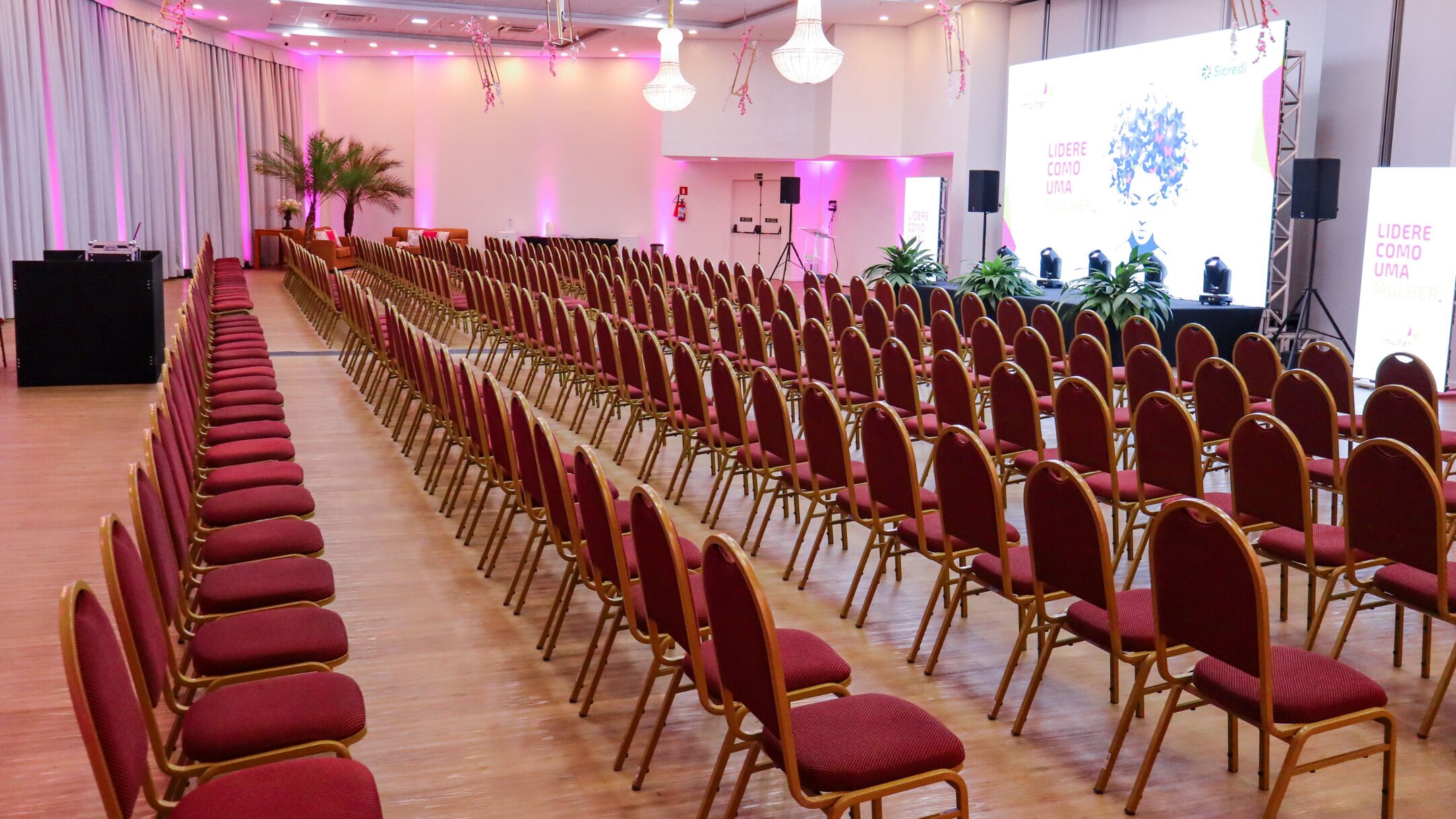 A conference room with rows of red chairs and a stage with a screen displaying text.