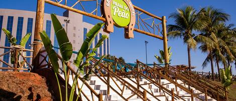 Entrada de un hotel con un letrero que dice 'Barreitos Park Hotel Praia do Peão', rodeada de palmeras y una escalera.
