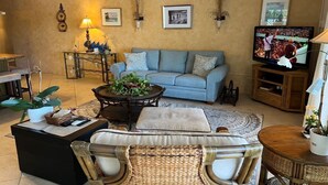 A cozy living room with a light blue sofa, a round coffee table with plants, a wicker chair, and a television on a wooden stand. - Canal View Summer Escape With Dock, Hot Tub and Cabana Club Access (Key Colony Beach, Marathon)