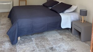 Een slaapkamer met een bed, nachtkastje, lamp, houten kapstok en een radiator.
