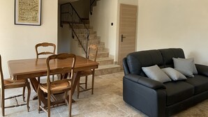 Een eethoek met een houten tafel en stoelen, een zwarte leren bank en een trap naar een andere kamer.