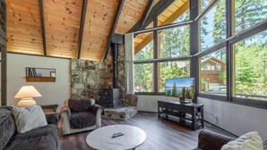 A cozy living room with a stone fireplace, large windows, and wooden beams. - Rim Drive Lookout (Tahoe Vista)