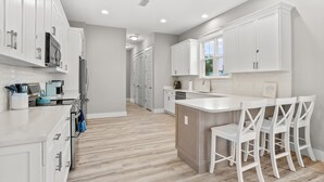 Une cuisine moderne avec des meubles blancs, un îlot central doté de tabourets de bar et un plancher en bois.