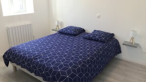 A bedroom with a bed, two bedside tables, a window, and a radiator.